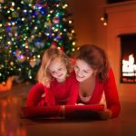 Mother and young daughter reading a book near a Christmas tree